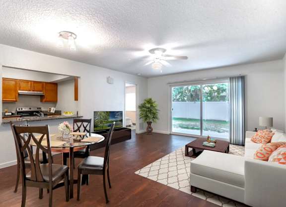 A living room with a couch, a dining table with chairs, and a kitchen area with a countertop and cabinets at Academy on Dean Woods Apartments, Florida, 32825