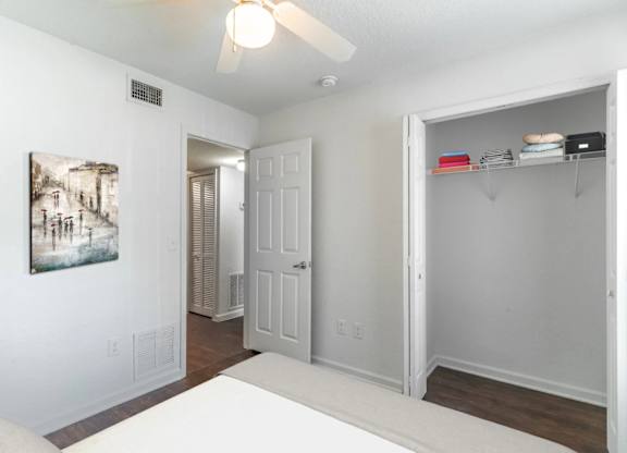 A white bedroom with a bed, a ceiling fan, and a painting on the wall at Academy on Dean Woods Apartments, Orlando, Florida