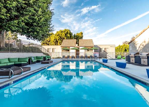 A large outdoor swimming pool with a sun lounger and trees in the background.