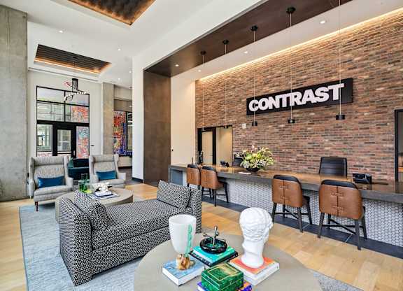 A living room with a grey couch and a brick wall with the word CONTRAST on it.