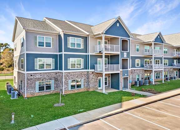 A large apartment complex with multiple balconies and a parking lot in front.