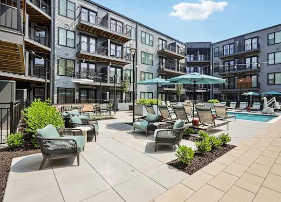 A sunny day at a modern apartment complex with a pool and lounge chairs.