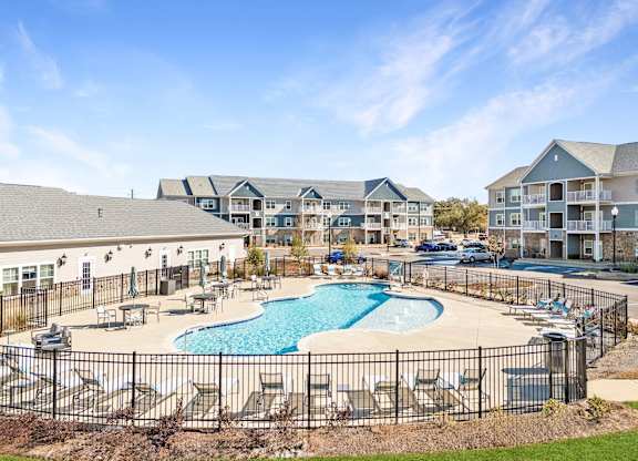 A large outdoor pool surrounded by a black fence and lounge chairs.