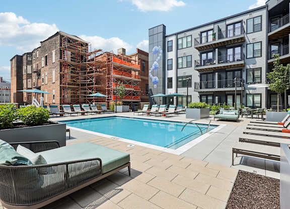 A pool surrounded by lounge chairs and apartment buildings.