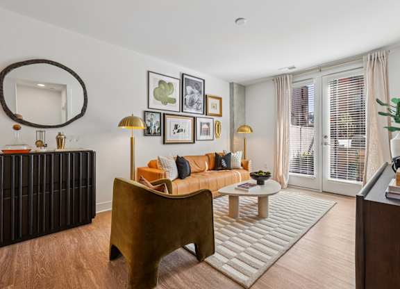 Modern living room at Contrast OTR apartments in Cincinnati, OH with tan leather sofa, gallery wall decor, and warm lighting.