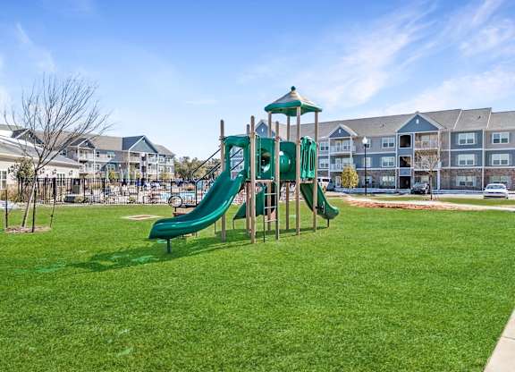 A green slide in a playground with apartment buildings in the background.