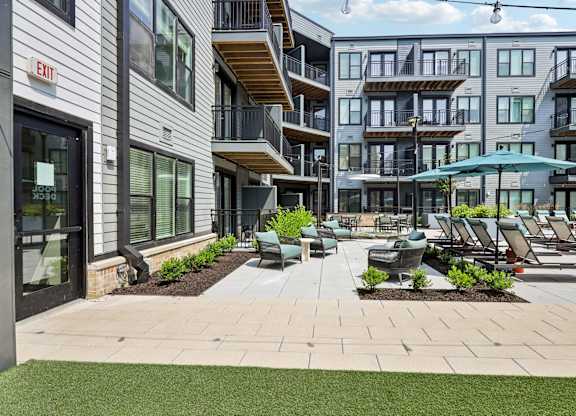 A patio area with chairs and umbrellas in front of apartment buildings.