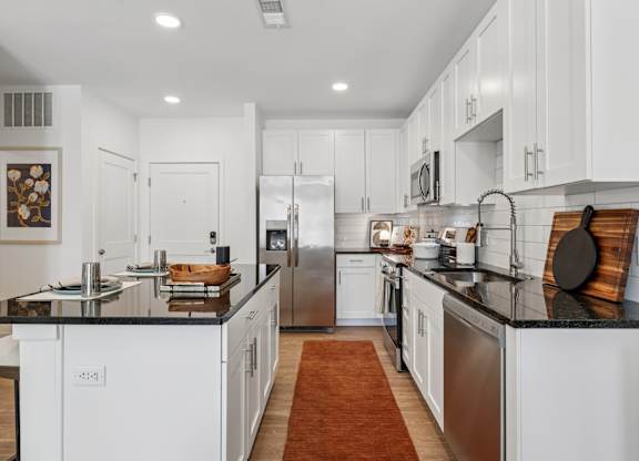 Sleek kitchen at Contrast OTR apartments in Cincinnati, OH with a large center island, modern lighting, and white shaker cabinets.