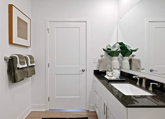 Modern bathroom at Contrast OTR in Cincinnati, OH featuring glass shower, granite countertops, and sleek white cabinetry.