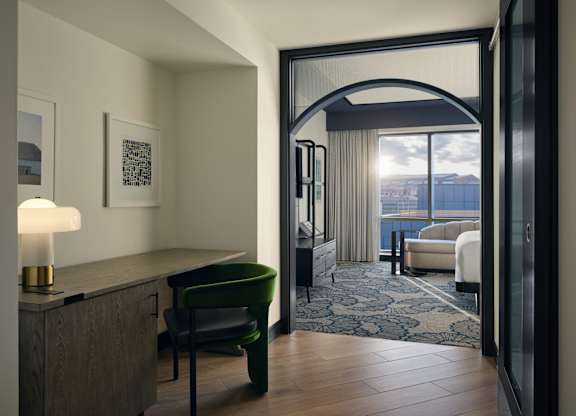 A room with a green chair and a lamp on a wooden table.