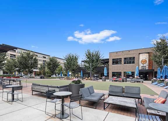 a patio area with tables and chairs and a lawn in front of a building