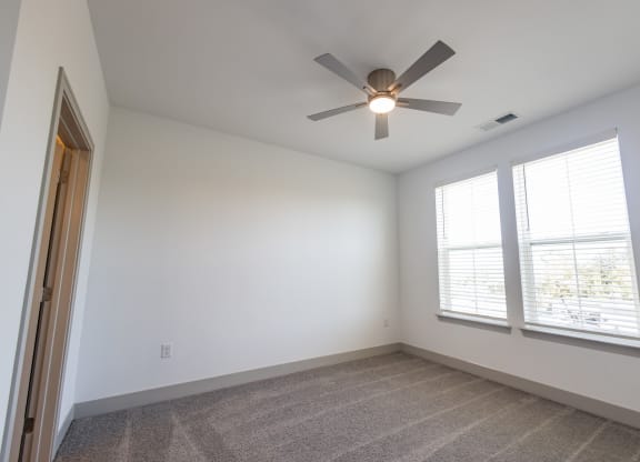 an empty room with a ceiling fan and two windows