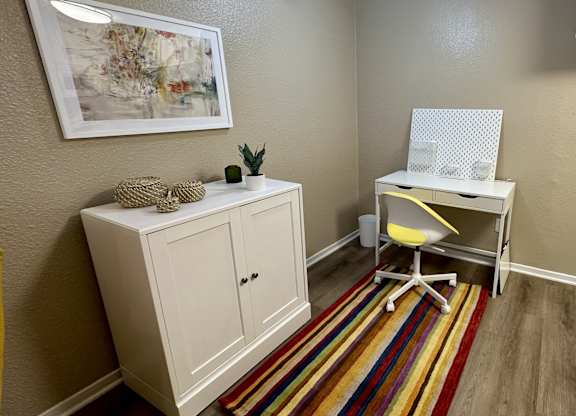 A white desk with a yellow chair and a white cabinet with a plant on top.