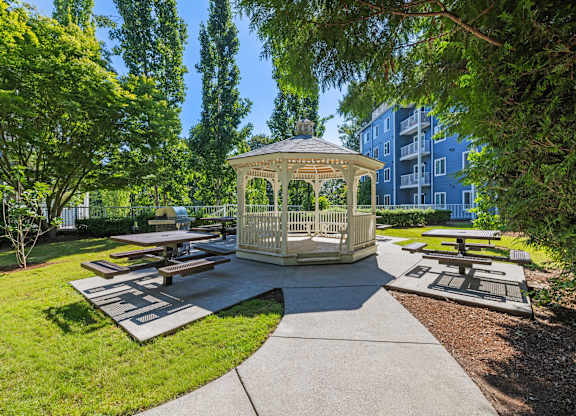 A gazebo is surrounded by picnic tables in a park.