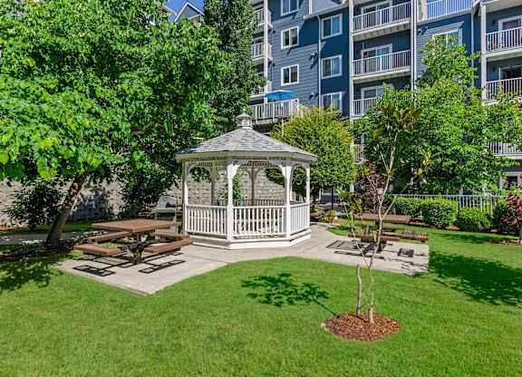 A gazebo is surrounded by a grassy area and trees.