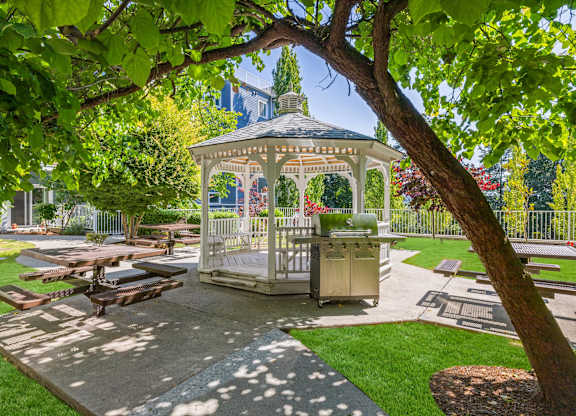 A gazebo is surrounded by picnic tables and green trees.