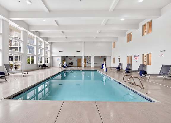 A large indoor swimming pool with lounge chairs and windows.