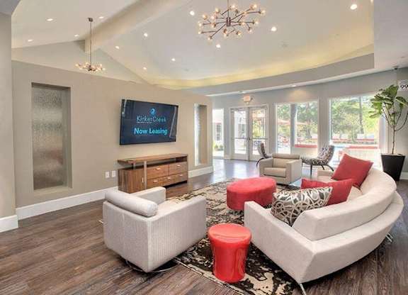 A living room with a white couch, a red ottoman, and a chandelier.