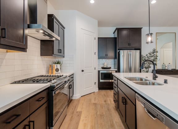 Large Kitchen with Stainless Steel Appliances, Wood-Style Flooring, White Tile Backsplash, Quartz Countertops, Dark Cabinets, and Stylish Decor at Crocker Village – Single Family Homes, Sacramento ? 