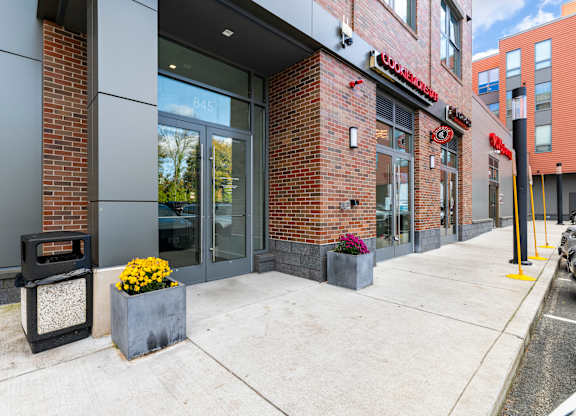 A brick building with a red sign on the front. at Trio Newton Apartments, Newton, MA, 02460