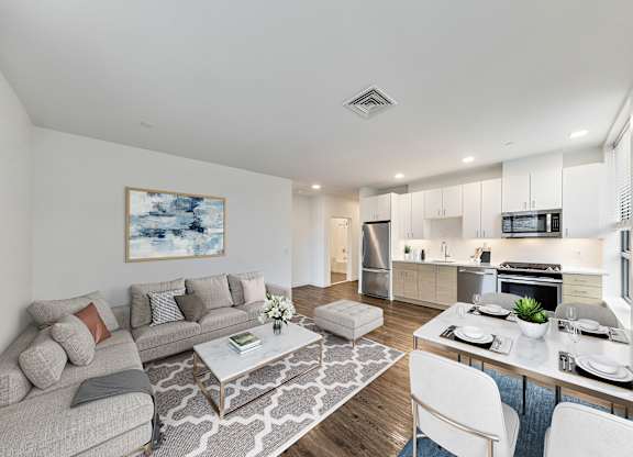A modern living room with a grey sofa, a coffee table, and a dining table set for two. at Trio Newton Apartments, Massachusetts