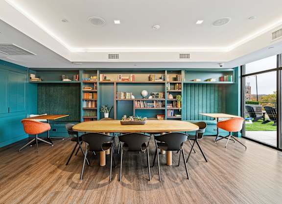 A room with a round table surrounded by chairs and a bookshelf filled with books at Trio Newton Apartments, Newton, 02460