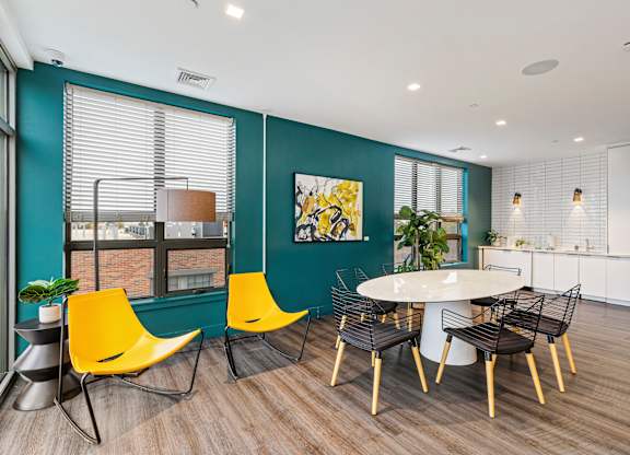 A room with a white table and yellow chairs. at Trio Newton Apartments, Apartments, Newton, MA