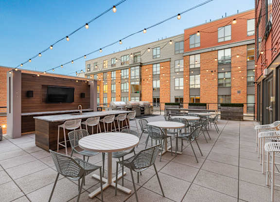 A patio with tables and chairs and a TV on a stand. at Trio Newton Apartments, Newton