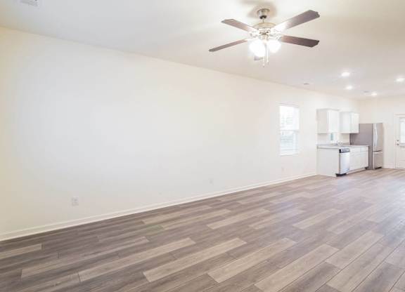 an empty living room with a ceiling fan and a kitchen
