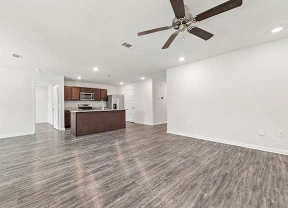 Open-concept kitchen and living area with gray wood-look flooring, brown cabinets, and a ceiling fan.