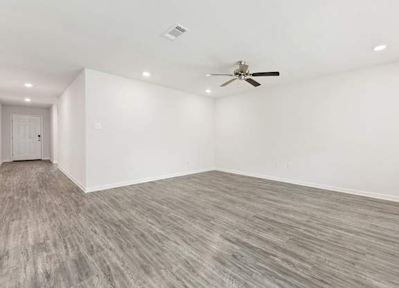 Empty room with gray wood-look flooring, white walls, ceiling fan, and recessed lighting.