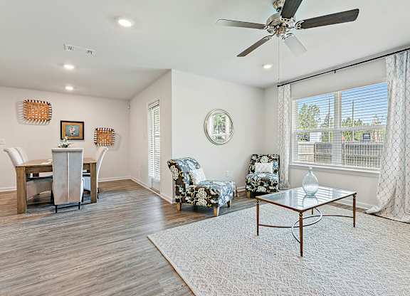 Interior view of a living and dining area with floral armchairs, glass coffee table, and wooden dining set.