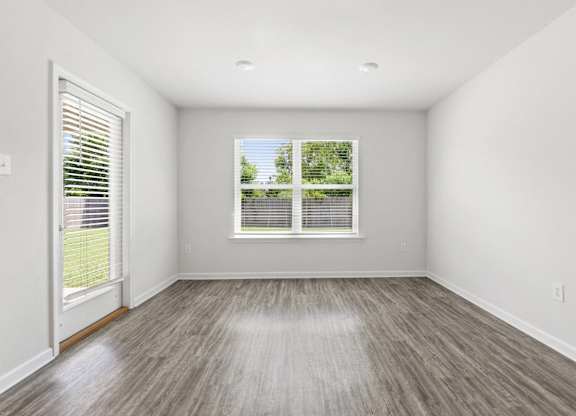 Empty room with gray wood-look flooring, white walls, a window with blinds, and a door leading outside.