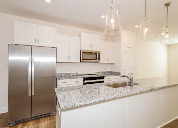 Townhouses for Rent in Charlotte, NC - Loso Walk - Modern Kitchen with Granite Countertops, a Kitchen Island, Hanging Lights, White Cabinetry, Stainless Steel Appliances, and Luxury Vinyl Plank Flooring