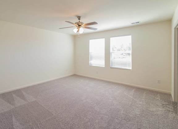 an empty living room with a ceiling fan and two windows
