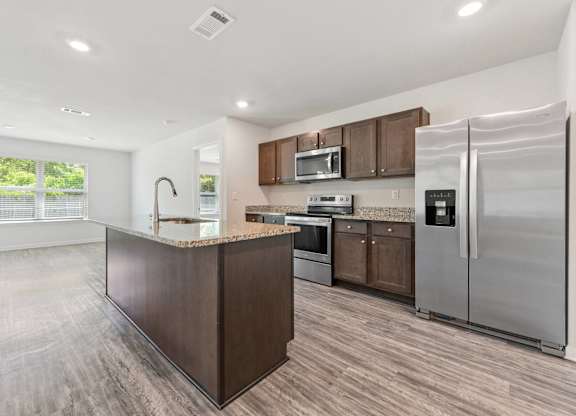 Modern kitchen with island, stainless steel appliances, and wood-look flooring.