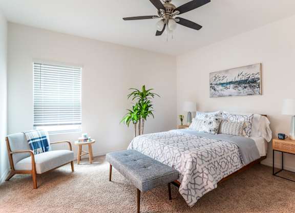 Bright, modern bedroom with geometric bedding, upholstered bench, armchair, and ceiling fan.