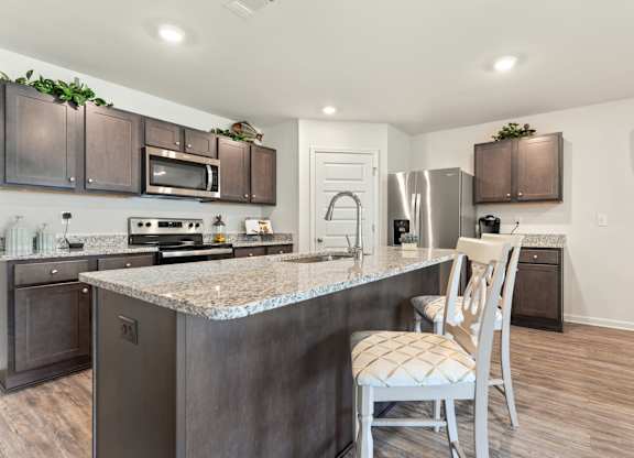 Modern kitchen with granite island, stainless steel appliances, and dark wood cabinets.