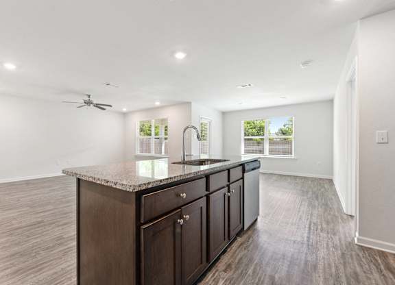 Modern kitchen island with granite countertop, dark wood cabinets, stainless steel sink and dishwasher in a bright, open-concept living space.