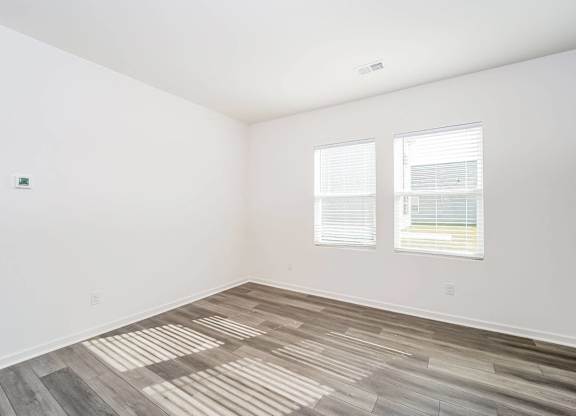 an empty room with wood flooring and two windows
