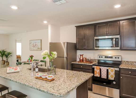 Modern kitchen with granite countertops, dark wood cabinets, stainless steel appliances, and island with seating.