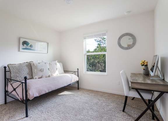 Bright living room with daybed, desk, and window overlooking trees.