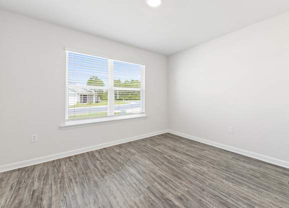Empty room with gray wood flooring, white walls, ceiling fan, and window.