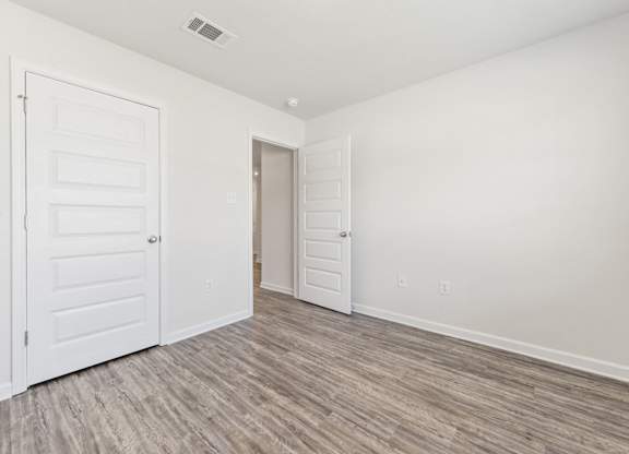 Empty white room with wood-look flooring, two paneled doors, and an open doorway.
