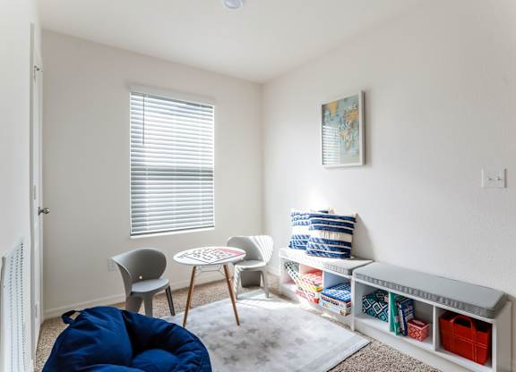 Bright, modern bedroom with a blue beanbag chair, small table with chairs, and a storage bench filled with toys and books.