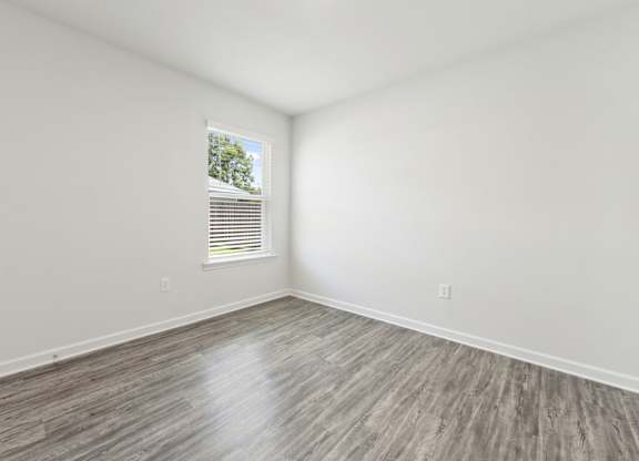 Empty room with gray wood-look flooring, white walls, and a window with blinds.
