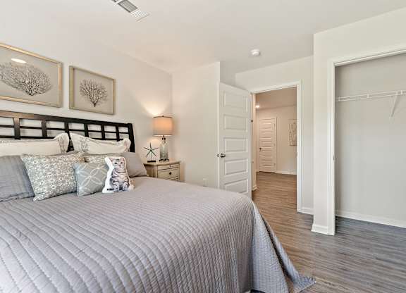 Bedroom with gray quilt, decorative pillows, open closet, and doorway to another room.