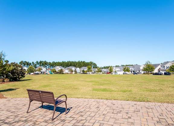 a park bench on a brick sidewalk next to a grass field