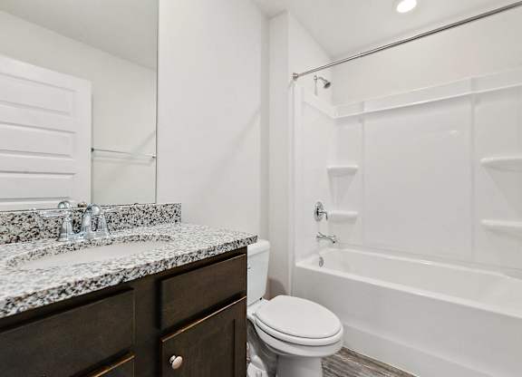 Modern bathroom with granite countertop, dark wood vanity, toilet, and white bathtub-shower combination.