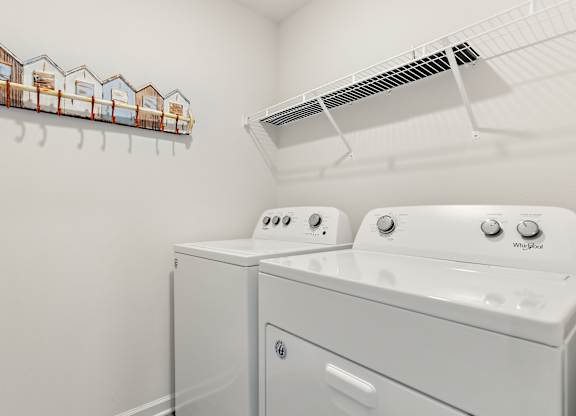 Laundry room with white Whirlpool washer and dryer, wire shelf, and beach hut-themed coat rack.